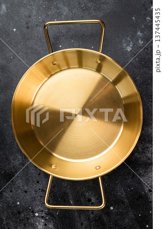 Round golden skillet with side handles on dark stone texture, overhead cookware background for restaurant and home kitchen Round golden skillet with side handles on dark stone texture, overhead cookware background for restaurant and home kitchen 137445435