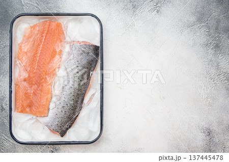 Raw salmon fillet with skin on ice in metal container. High quality fresh seafood fish on light textured background. 137445478