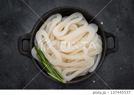 Raw calamari squid loops on black textured surface with herbs offering minimal ocean seafood ingredient concept for culinary design Raw calamari squid loops on black textured surface with herbs offering minimal ocean seafood ingredient concept for culinary design 137445537