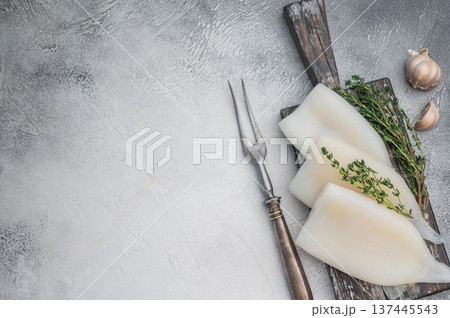 Raw calamari arranged with herbs on weathered wood against a gray stone backdrop ideal for culinary seafood stock concepts. 137445543
