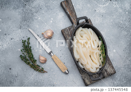 Raw squid rings arranged in rustic black dish with herbs on gray stone backdrop perfect for seafood cuisine and recipes. 137445548