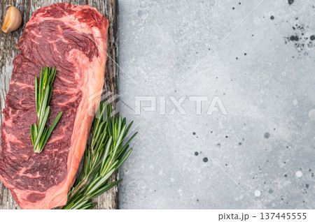Raw striploin steak with rosemary on a rustic wooden board over light concrete background perfect for grilling cooking and food styling shots Raw striploin steak with rosemary on a rustic wooden board over light concrete background perfect for grilling cooking and food styling shots 137445555