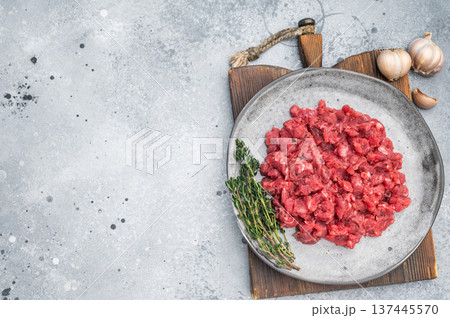 Raw chopped beef veal meat served with herbs on rustic plate against textured concrete backdrop perfect for culinary ads and protein food visuals. Raw chopped beef veal meat served with herbs on rustic plate against textured concrete backdrop perfect for culinary ads and protein food visuals. 137445570