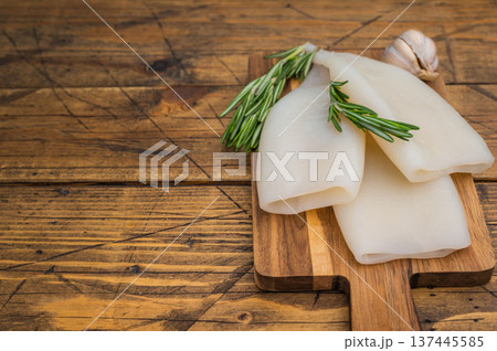 Raw calamari and fresh rosemary on vintage wood board captured for culinary design seafood menus and Mediterranean style visuals 137445585