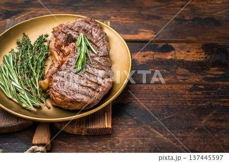 Cooked New York strip steak with rich marbling served with fresh thyme and rosemary on warm wooden textured board Cooked New York strip steak with rich marbling served with fresh thyme and rosemary on warm wooden textured board 137445597