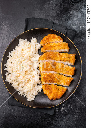 Delicious katsu style dish, featuring a perfectly cooked chicken meat cutlet served alongside steamed rice for a balanced meal. black background. top view Delicious katsu style dish, featuring a perfectly cooked chicken meat cutlet served alongside steamed rice for a balanced meal. black background. top view 137445762