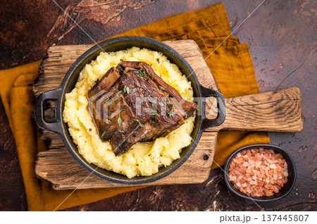 Close-up of tender beef short ribs, beautifully caramelized and resting on a bed of creamy mashed potatoes, creating an inviting culinary scene. brown background. top view 137445807