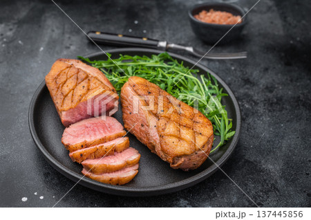Gourmet grilled duck fillet with crispy skin and tender slices served on black plate over textured dark surface ideal for food photography. Gourmet grilled duck fillet with crispy skin and tender slices served on black plate over textured dark surface ideal for food photography. 137445856