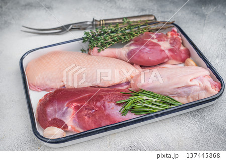 Raw duck parts breast wing thigh and fillet with herbs and garlic in enamel tray on light stone background with vintage fork for food stock images. Raw duck parts breast wing thigh and fillet with herbs and garlic in enamel tray on light stone background with vintage fork for food stock images. 137445868