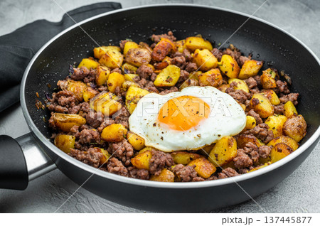 Beef hash with fried potatoes, ground beef and sunny egg in skillet on gray surface with dark napkin, perfect for rustic cooking themes. 137445877