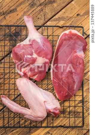Fresh uncooked duck cuts breast fillet thigh and wingarranged on cooling grid against scratched wood surface perfect for culinary preparation visuals. 137445889