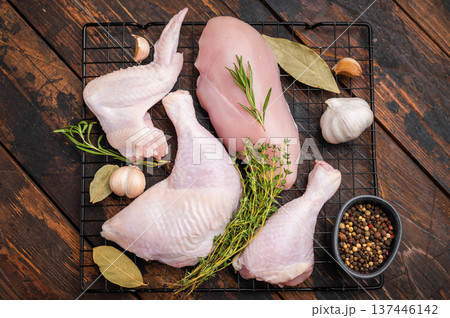 Raw chicken cuts (breast, leg, wing) on a rack with thyme, rosemary, garlic, and peppercorns on dark rustic wood. Ready for seasoning. 137446142