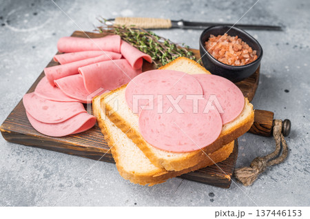 Slices of pink bologna lunch meat on toasted white bread with rock salt and thyme on a wooden board. Grey background with copy space. Slices of pink bologna lunch meat on toasted white bread with rock salt and thyme on a wooden board. Grey background with copy space. 137446153