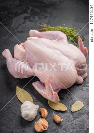 Raw whole chicken with fresh thyme and garlic cloves on a dark, black textured stone background. Preparing to cook poultry. Raw whole chicken with fresh thyme and garlic cloves on a dark, black textured stone background. Preparing to cook poultry. 137446154