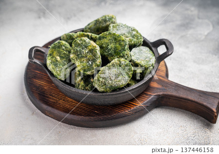 Overhead shot of frozen spinach blocks in a cast iron skillet on a wooden board. Grey textured background with copy space. 137446158
