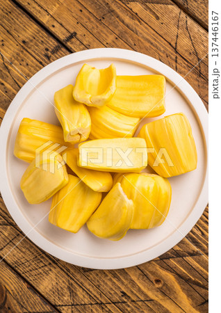 Sweet, golden yellow jackfruit pods (bulbs) served on a white plate on a rustic wooden table. Fresh, tropical fruit snack. 137446167