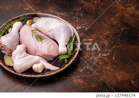 The promise of a perfect roast: prime raw poultry cuts rest with fragrant rosemary, thyme, and garlic on a deep, earthen plate, awaiting their culinary transformation. 137446174