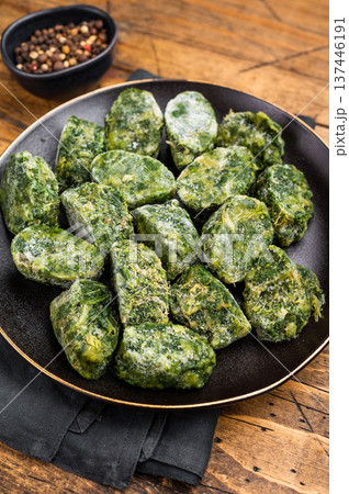 Raw, nutritious frozen spinach blocks on a dark plate, ready for thawing and cooking. Traditional rustic food photography. Raw, nutritious frozen spinach blocks on a dark plate, ready for thawing and cooking. Traditional rustic food photography. 137446191