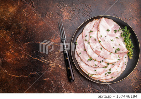 Slices of Italian Pancetta Arrotolata with thyme on a black plate, next to a vintage fork on a dark brown background. 137446194
