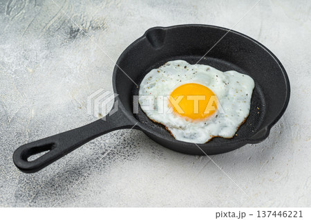 Hot frying egg in cast iron pan, glowing yolk and white contrast on bright background. Classic brunch concept with simple rustic styling.. Hot frying egg in cast iron pan, glowing yolk and white contrast on bright background. Classic brunch concept with simple rustic styling.. 137446221