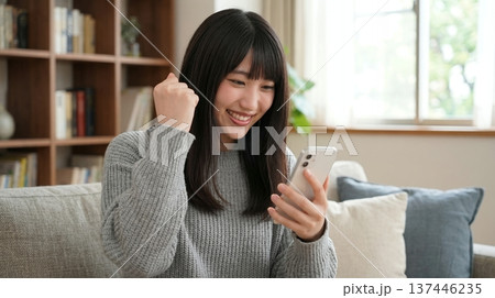 スマホを見てガッツポーズをする若い女性 137446235