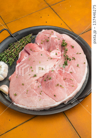 Raw bone in pork shoulder in round pan with thyme and garlic on yellow tiled background fresh meat prepared for roasting and slow cooking Raw bone in pork shoulder in round pan with thyme and garlic on yellow tiled background fresh meat prepared for roasting and slow cooking 137446275