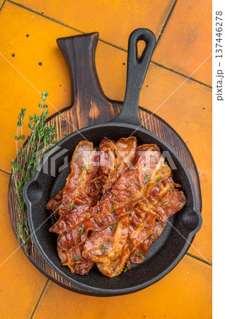 Glossy roasted Streaky bacon strips served in black skillet with fresh thyme over rustic yellow surface ideal for menus and food ads. Glossy roasted Streaky bacon strips served in black skillet with fresh thyme over rustic yellow surface ideal for menus and food ads. 137446278