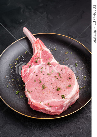 Juicy raw pork chop with bone in, waiting to be transformed into a delicious centerpiece for your table. black background. top view Juicy raw pork chop with bone in, waiting to be transformed into a delicious centerpiece for your table. black background. top view 137446533