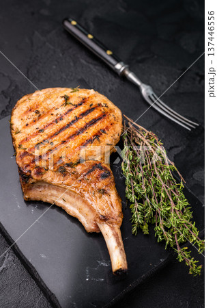 Savory bone in pork chop steak, beautifully charred and ready to impress at your next barbecue gathering. black background. top view Savory bone in pork chop steak, beautifully charred and ready to impress at your next barbecue gathering. black background. top view 137446556