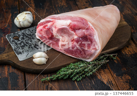 Raw pork knuckle with forged cleaver garlic and thyme on rustic wooden background perfect for butchery themes and recipe imagery. Raw pork knuckle with forged cleaver garlic and thyme on rustic wooden background perfect for butchery themes and recipe imagery. 137446655
