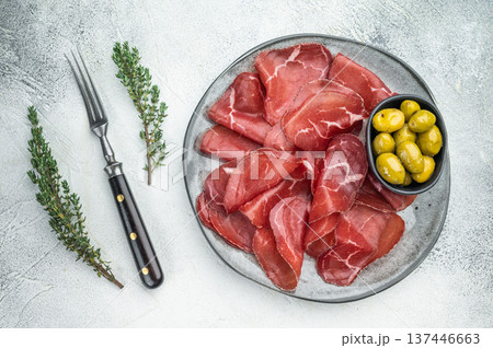 Gourmet Italian bresaola charcuterie with green olives and herbs, presented on a stone textured background for elegant flat lay. Gourmet Italian bresaola charcuterie with green olives and herbs, presented on a stone textured background for elegant flat lay. 137446663