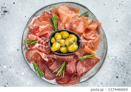 Bresaola, prosciutto and coppa slices with green olives on a rustic gray background, perfect for Mediterranean food visuals. 137446669