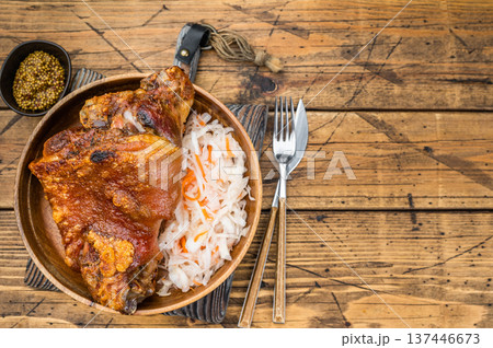 Crispy roasted pork knuckle shank with golden crackling rind served with fermented cabbage slaw on rustic wooden background. 137446673