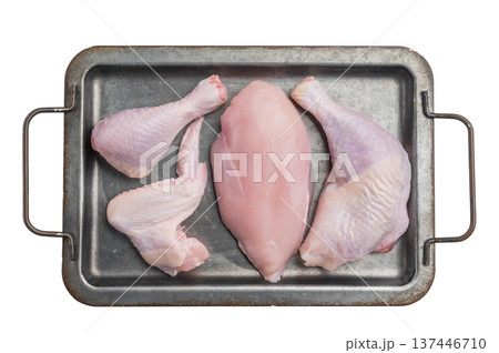 Raw chicken cuts: breast, wing, drumstick, and leg quarter, displayed on a rustic metal tray on a white surface. High-protein meat. 137446710