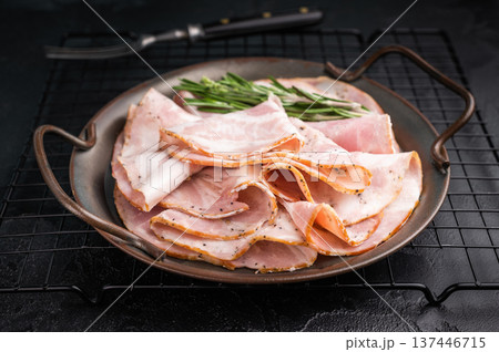 Slices of Italian Pancetta Arrotolata with rosemary in a metal dish, next to a vintage fork on a dark background with copy space. 137446715