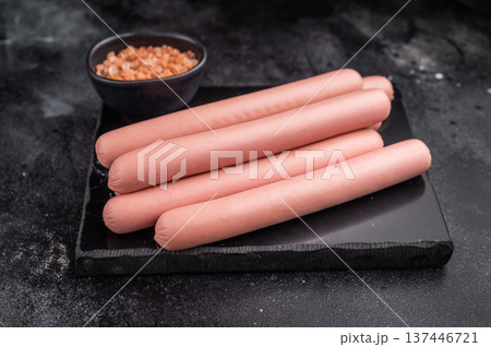 Four raw pink hot dog sausages (frankfurters/wieners) on a contrasting dark stone background with Himalayan salt. Copy space. 137446721