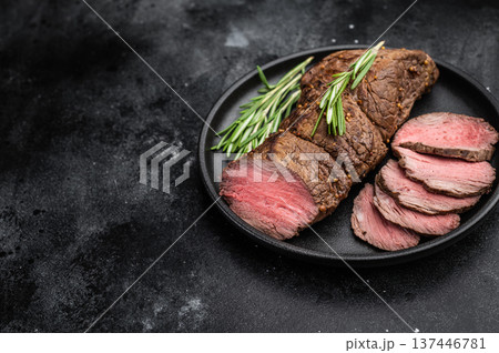 Classic roast beef meat sliced into portions. Medium rare baked beef cut with herbs on dark stone background. Classic roast beef meat sliced into portions. Medium rare baked beef cut with herbs on dark stone background. 137446781
