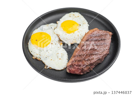 Classic American steak and eggs with beef steak and two sunny side fried eggs cooked in cast iron skillet on isolated background 137446837