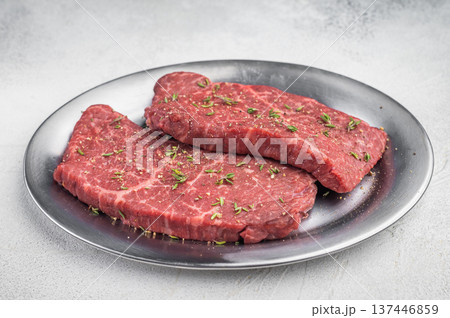 Raw chuck flatiron beef steaks with thyme leaves on metal serving plate flat lay on light gray background Raw chuck flatiron beef steaks with thyme leaves on metal serving plate flat lay on light gray background 137446859