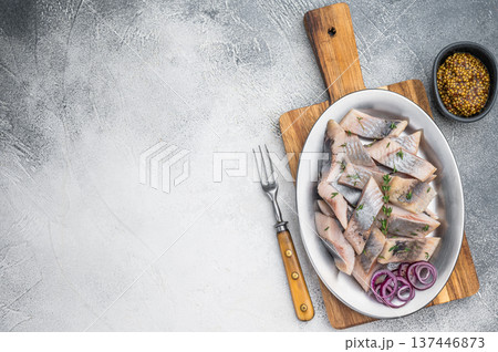 Salted and marinated herring pieces with red onion and thyme served in white dish on wooden board. Light stone background with copy space. 137446873