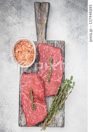 Uncooked chuck flatiron beef steaks with thyme sprigs and seasoning on vintage board overhead minimal composition 137446895