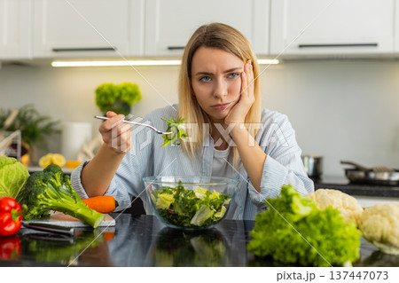 Young woman tired of strict keto diet refusing veggie salad in home kitchen feeling hungry and bored 137447073