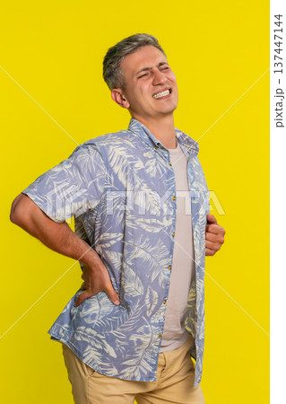 Adult man holding lower back straightening up with painful expression from strain or pinched nerve Adult man holding lower back straightening up with painful expression from strain or pinched nerve 137447144