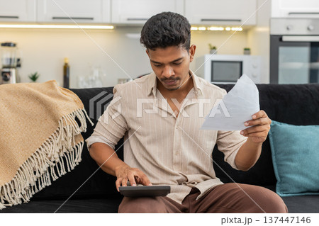 Indian man plans utility budget uses calculator holds bills squints and marks priorities for month Indian man plans utility budget uses calculator holds bills squints and marks priorities for month 137447146