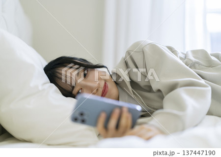 寝転んでスマートフォンの画面を見つめる若い女性 寝転んでスマートフォンの画面を見つめる若い女性 137447190