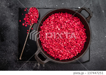 Crunchy freeze dried raspberry pieces used as topping and baking ingredient in iron skillet on dark background 137447251