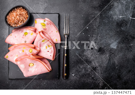 Mortadella Bolognese sausage slices with pistachios. black background. top view Mortadella Bolognese sausage slices with pistachios. black background. top view 137447471
