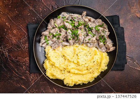Beef stroganoff with mashed potatoes, fresh greenery and savory mushroom sauce in a plate . brown background. top view Beef stroganoff with mashed potatoes, fresh greenery and savory mushroom sauce in a plate . brown background. top view 137447526