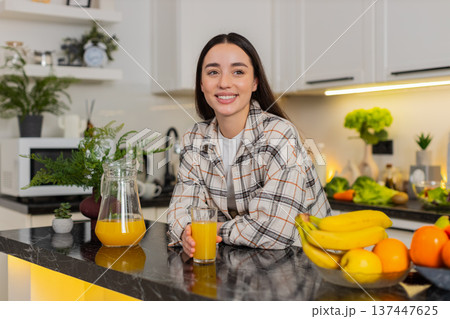 Young woman pours fresh orange juice from glass pitcher into tumbler in modern home kitchen, closeup Young woman pours fresh orange juice from glass pitcher into tumbler in modern home kitchen, closeup 137447625