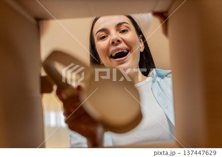 Young woman happily unpacking delivery box receiving new wireless headphones excited joyful smiling 137447629